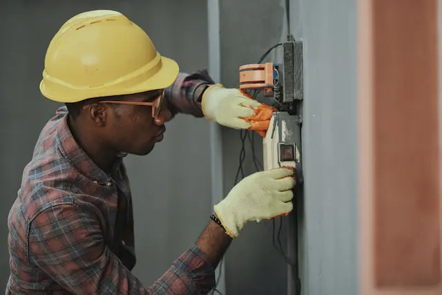 Man doing electrical work in a yellow construction hat and leather gloves.